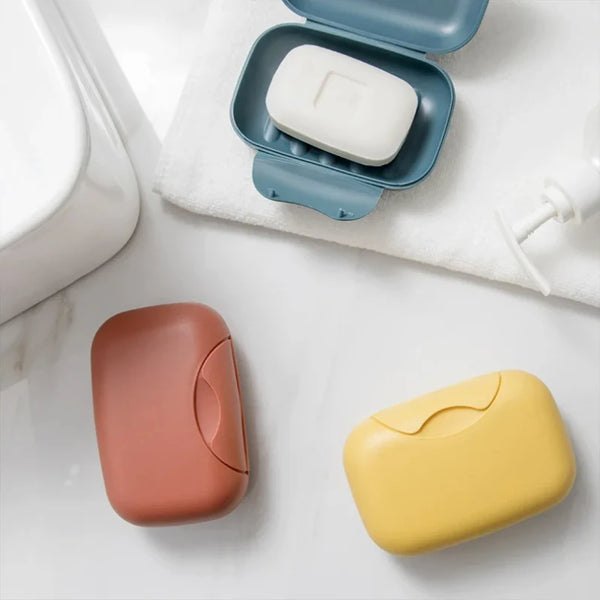 A collection of portable travel soap boxes in pink, white, and yellow are displayed on a white surface.