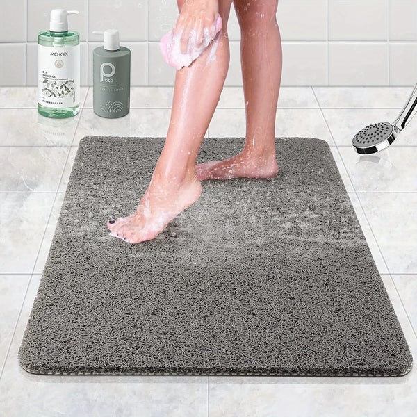 A person's legs are standing on a gray microfiber bathroom mat while using a foot scrubber.