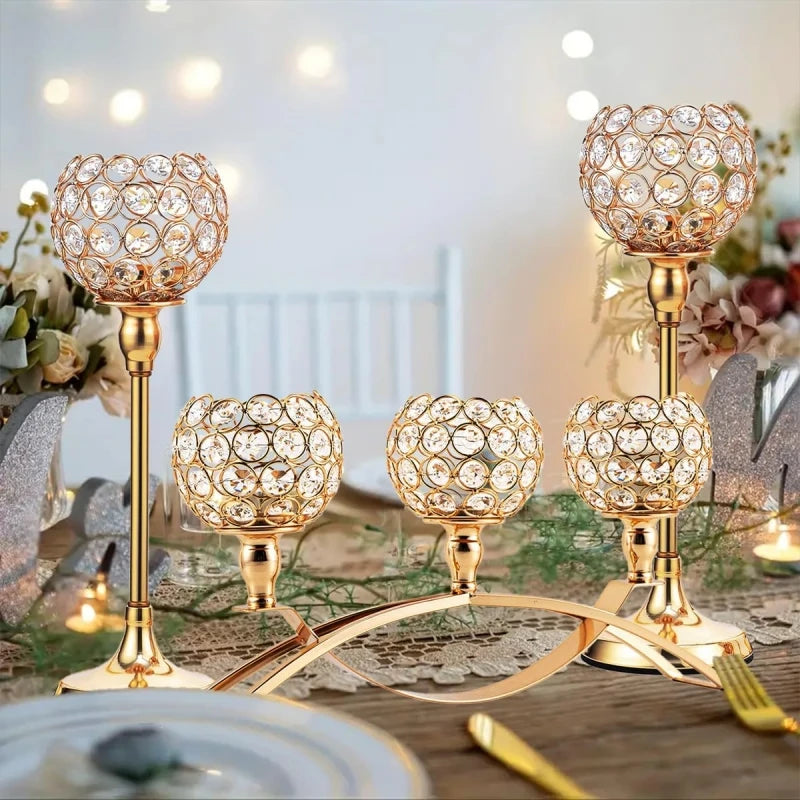 A set of gold crystal tealight candlesticks displayed on a wooden table with greenery.