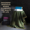 A stack of folded bath towels in teal, white, and purple rests on a green fabric drape.
