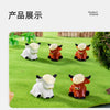 A display of resin highland cow figurines in various colors and poses on green grass.