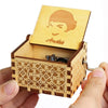 An antique wooden hand crank music box with a light wood casing and a carved face on the lid.