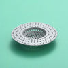 A circular, perforated kitchen sink drain strainer and hair catcher made of white plastic resting on a light green surface.