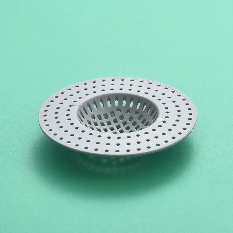 A circular, perforated kitchen sink drain strainer and hair catcher made of white plastic resting on a light green surface.