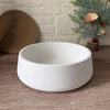 A white silicone resin mold bowl resting on a wooden surface next to a green branch.