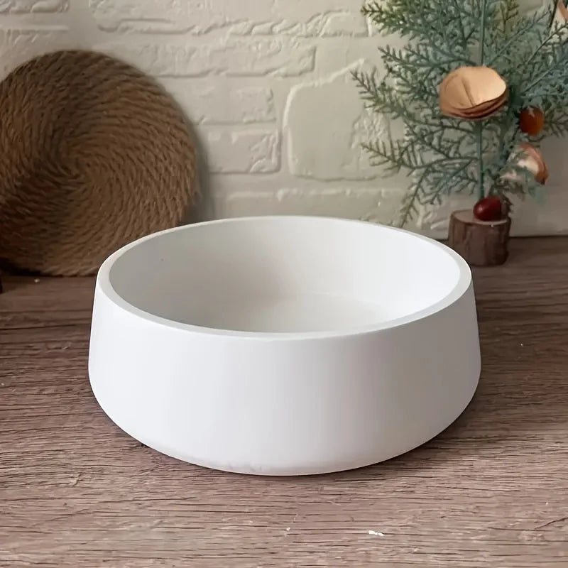 A white silicone resin mold bowl resting on a wooden surface next to a green branch.