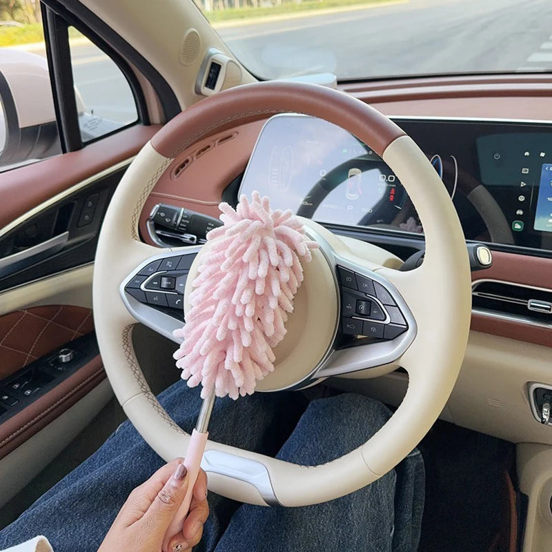 A hand holds a pink microfiber duster brush in the steering wheel of a car.