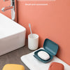 A portable travel soap box in yellow and terracotta colors is shown next to a white toilet and a towel.
