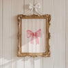 Pastel pink bow canvas wall art framed in gold on a white wooden wall