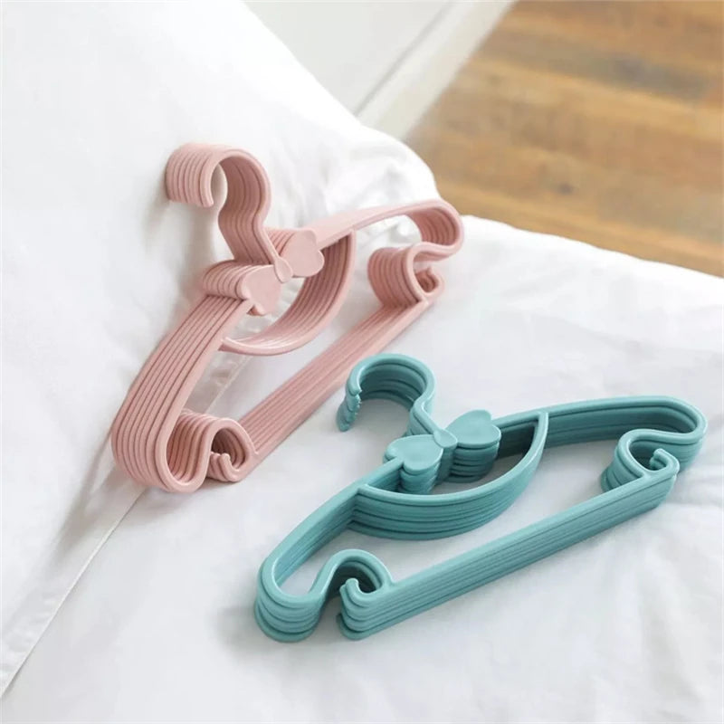 Two pink and teal plastic clothes hangers for kids and coats lying on a white sheet.