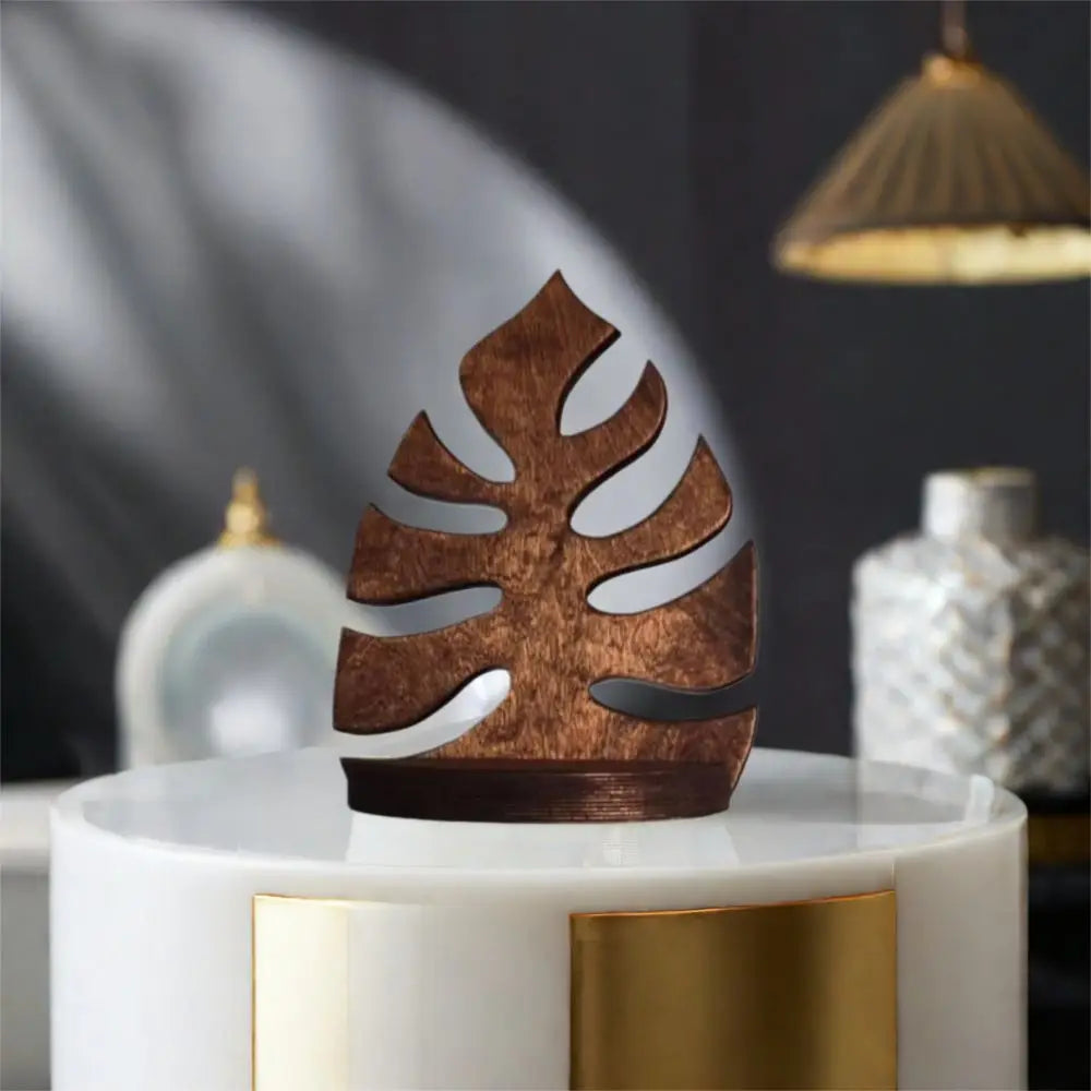 A wooden wall art frame shaped like a monstera leaf sits on a white pedestal.