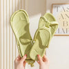 Une paire de tongs pliables en EVA vert clair, tenues par des mains sur un fond clair.