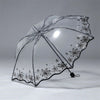 A clear, retro transparent folding umbrella decorated with black floral patterns.