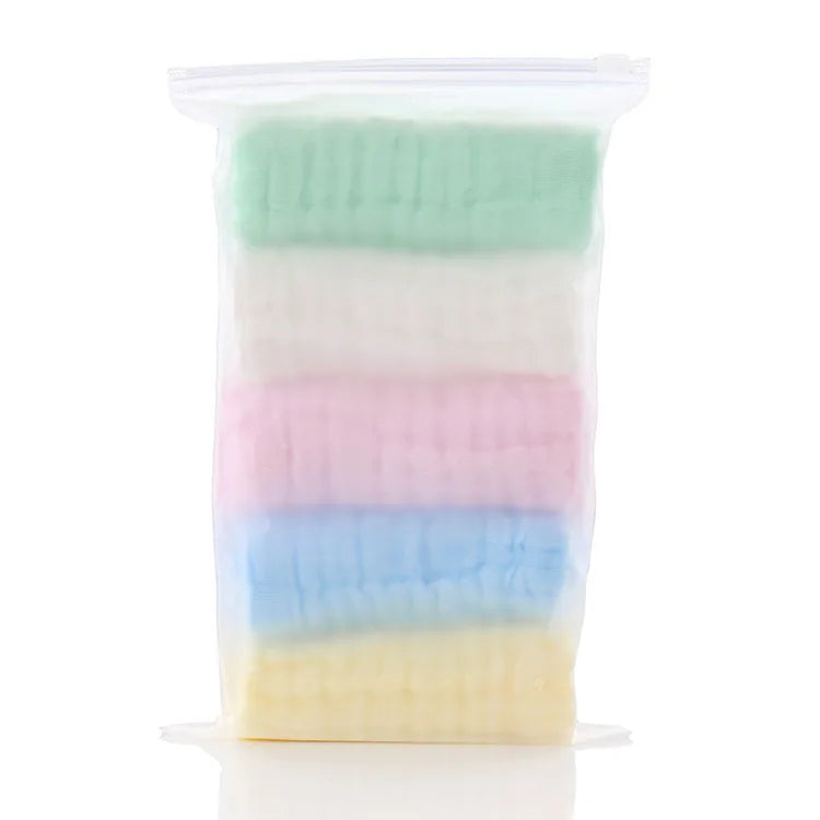 Una bolsa de plástico transparente con cinco toallitas orgánicas de algodón para bebé y cara de colores pastel apiladas.