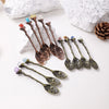 A collection of natural crystal spoons with various colors and shapes resting on a white surface next to a pine cone.