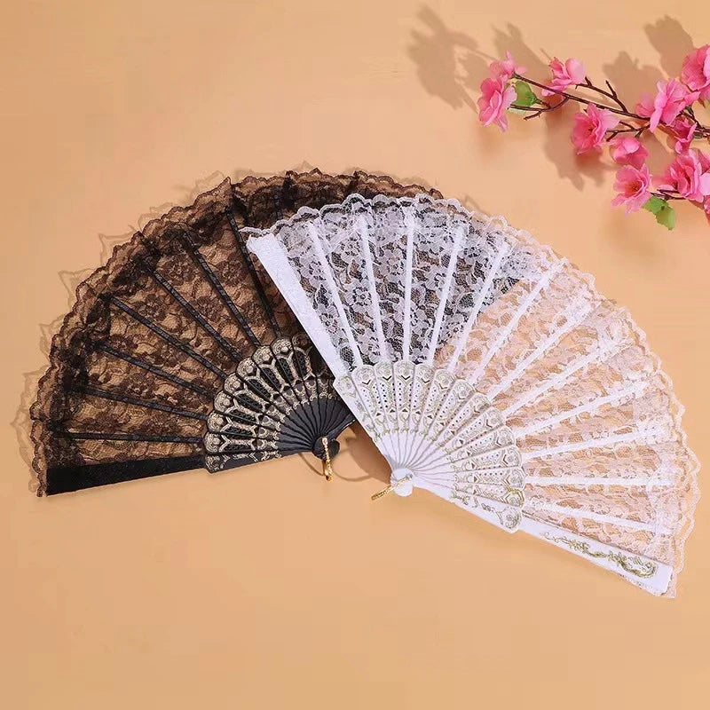 A pair of lace fabric folding hand fans in black and white resting on a beige surface.