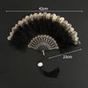 A black and gold lace fabric folding hand fan with a feathered edge and a tassel.