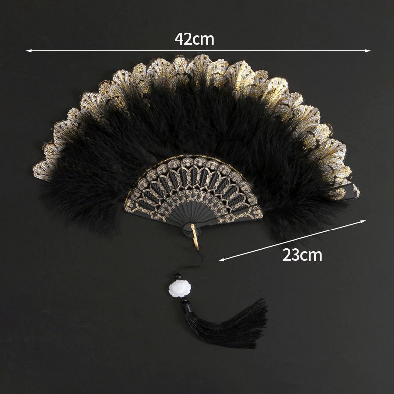 A black and gold lace fabric folding hand fan with a feathered edge and a tassel.