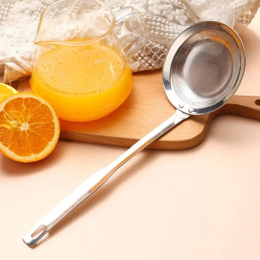 A stainless steel fat skimmer strainer is shown with orange juice and a slice of orange on a wooden board.