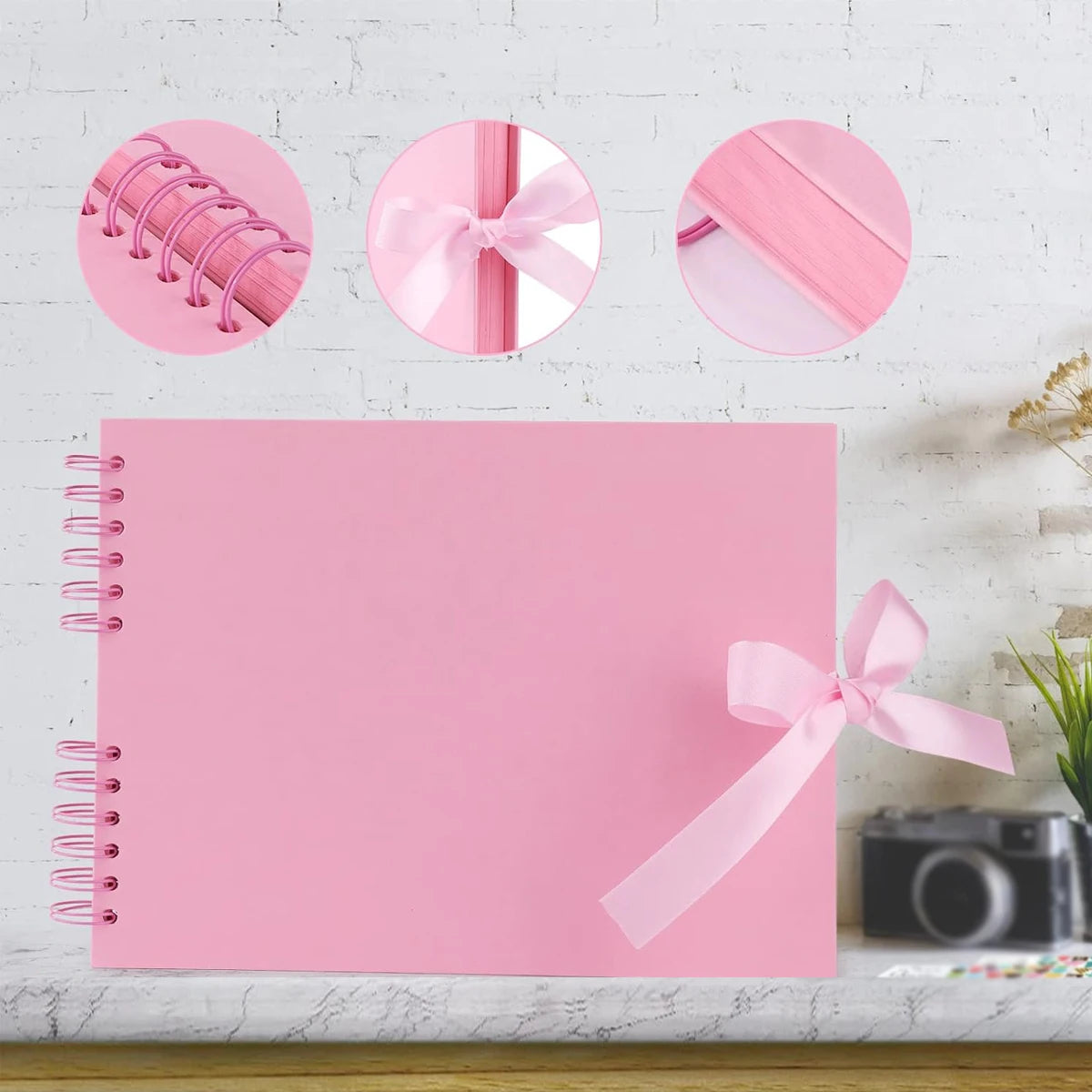 Cuaderno espiral rosa con lazos y un lazo rosa decorativo, sobre fondo de ladrillo blanco.