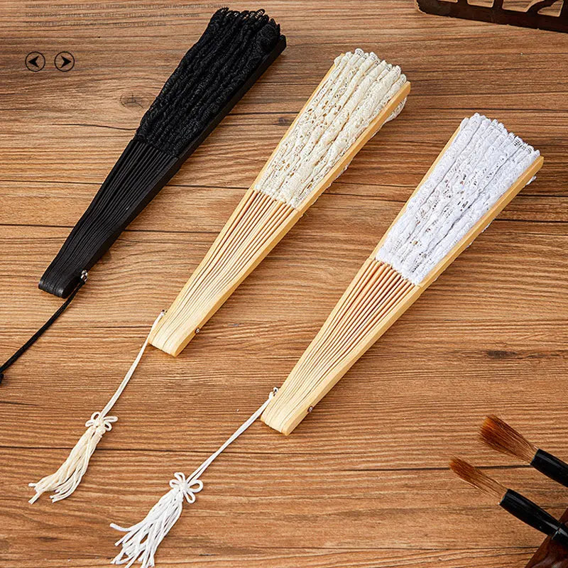 Three wooden folding hand fans are displayed on a wooden surface, showing black and natural colored lace patterns.