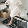 A child wearing a white bathrobe stands on a black pebble embossed bathroom rug.