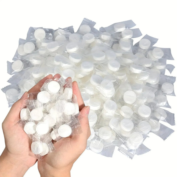 A hand holds a large quantity of disposable compressed wash wipes for face and body.