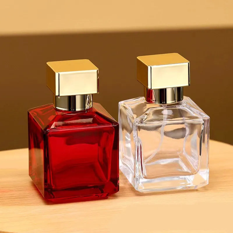 A clear glass perfume bottle with a gold cap and a red glass bottle are displayed on a wooden surface.