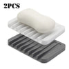 Two silicone soap dishes, one white and one gray, showing a self-draining design.