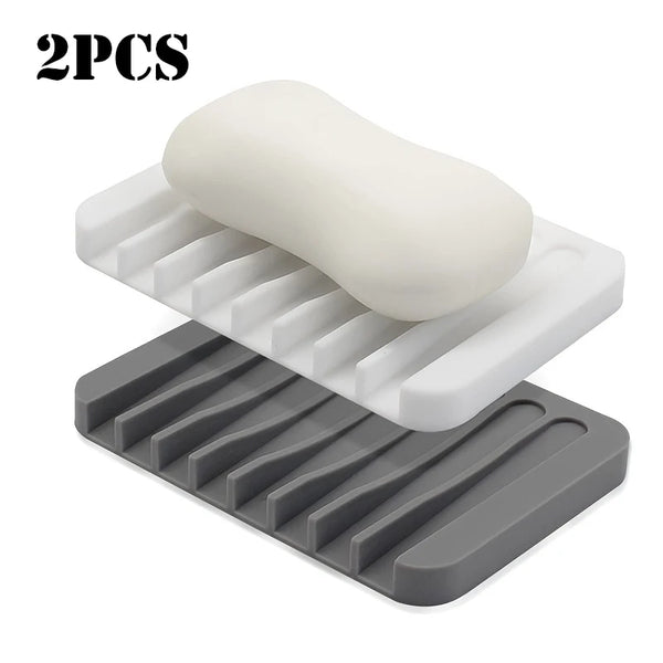 Two silicone soap dishes, one white and one gray, showing a self-draining design.