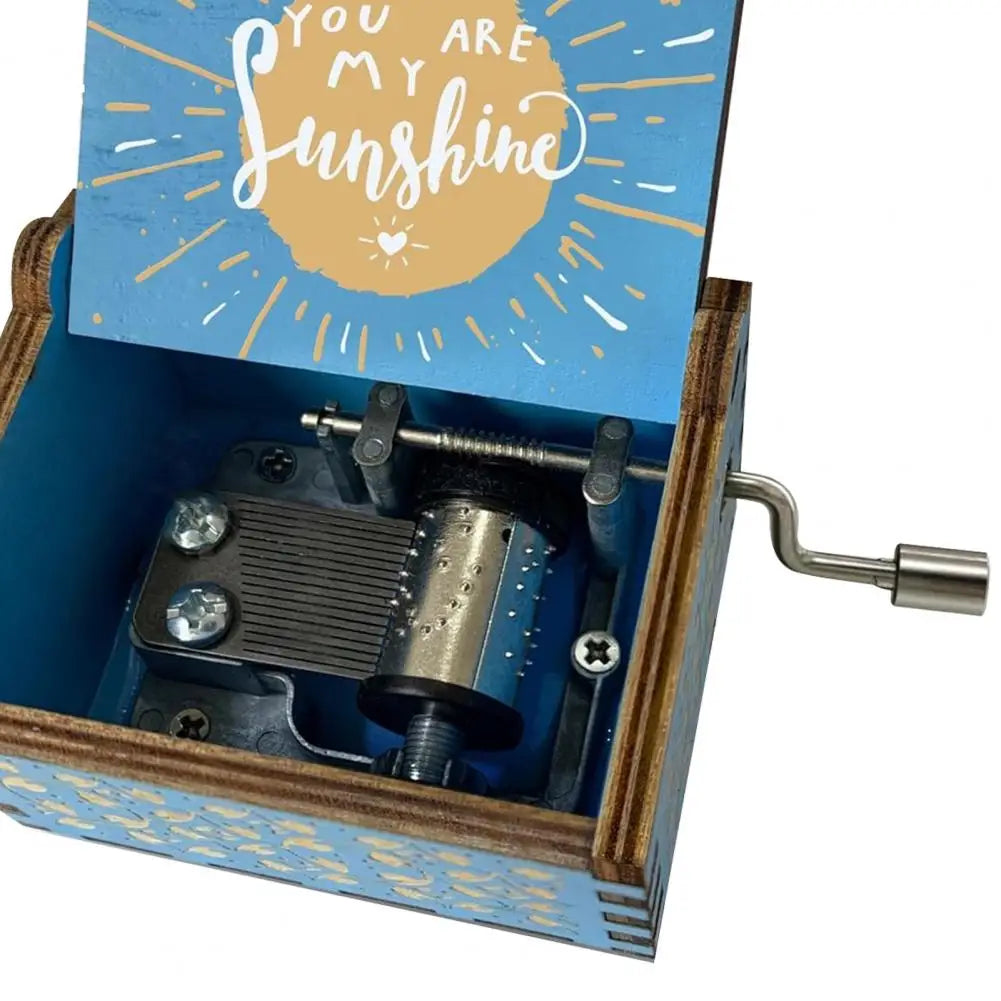 A mini wooden music box with a blue lid featuring the text You Are My Sunshine and an exposed hand crank mechanism.