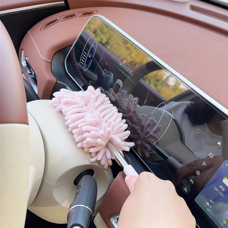 A close-up view of a pink extendable microfiber duster brush being used on the interior of a car