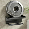 A black no-drill toilet paper holder with a storage shelf mounted on a gray tiled wall.