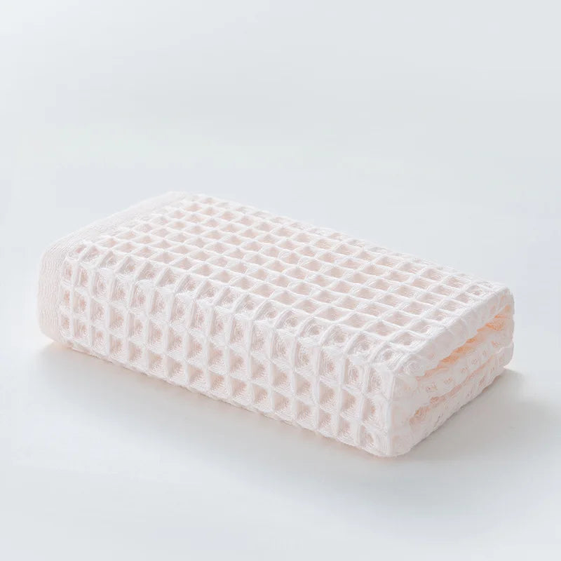 Rechteckliches rosa Waffel-Textur-Badetuch liegt flach auf einer weißen Oberfläche.