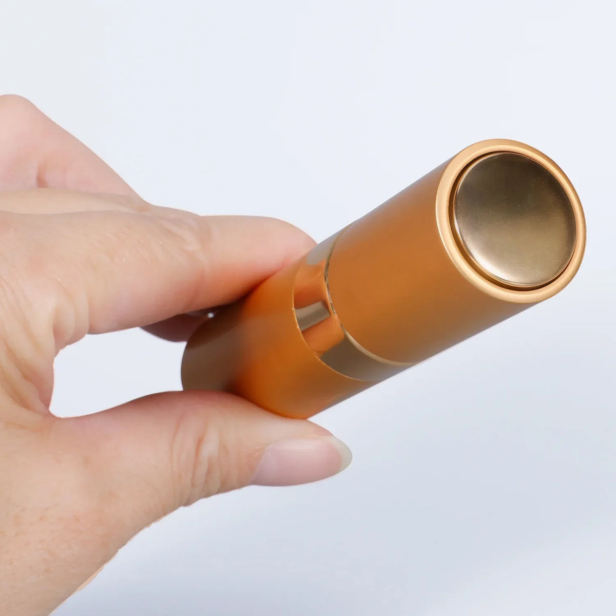 A hand is holding a gold-colored portable refillable perfume spray bottle.