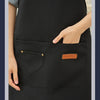 A close-up of a black all-purpose canvas apron with a chest pocket and a brand tag.