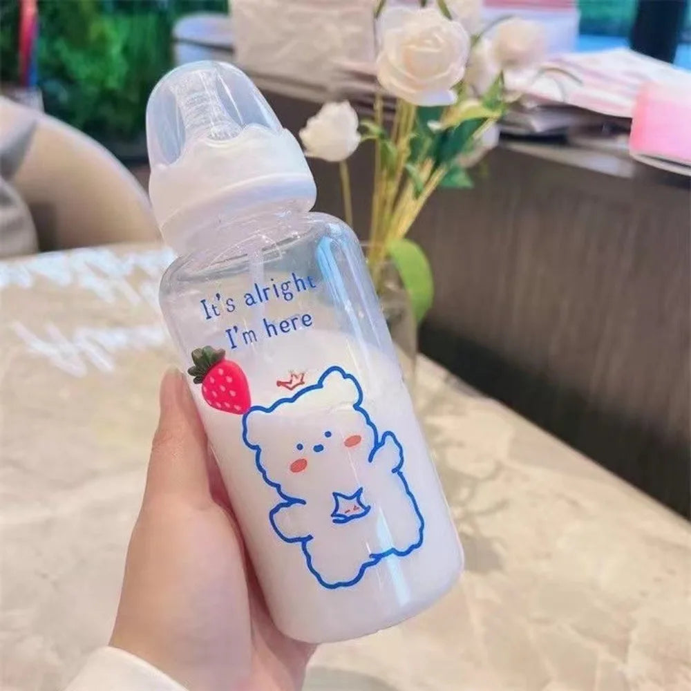 A hand holds a clear water bottle with a strawberry bear design and a white cap on a table.
