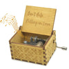 A vintage engraved wooden music box with a lid featuring the text Can't Help Falling in Love and a small metal mechanism insi