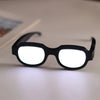 Black LED light up anime glasses with white lenses resting on a white surface.