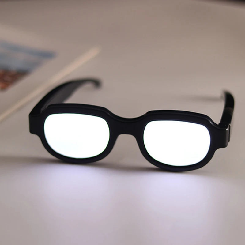 Black LED light up anime glasses with white lenses resting on a white surface.