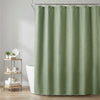 A light sage green waffle weave shower curtain hanging on a metal rod in a bathroom setting.