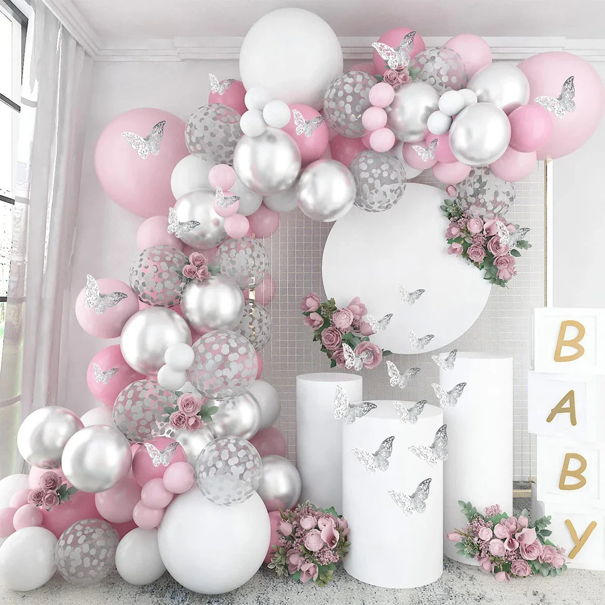 A pink and white balloon garland featuring heart shapes, glitter textures, and floral accents for a baby shower or celebratio