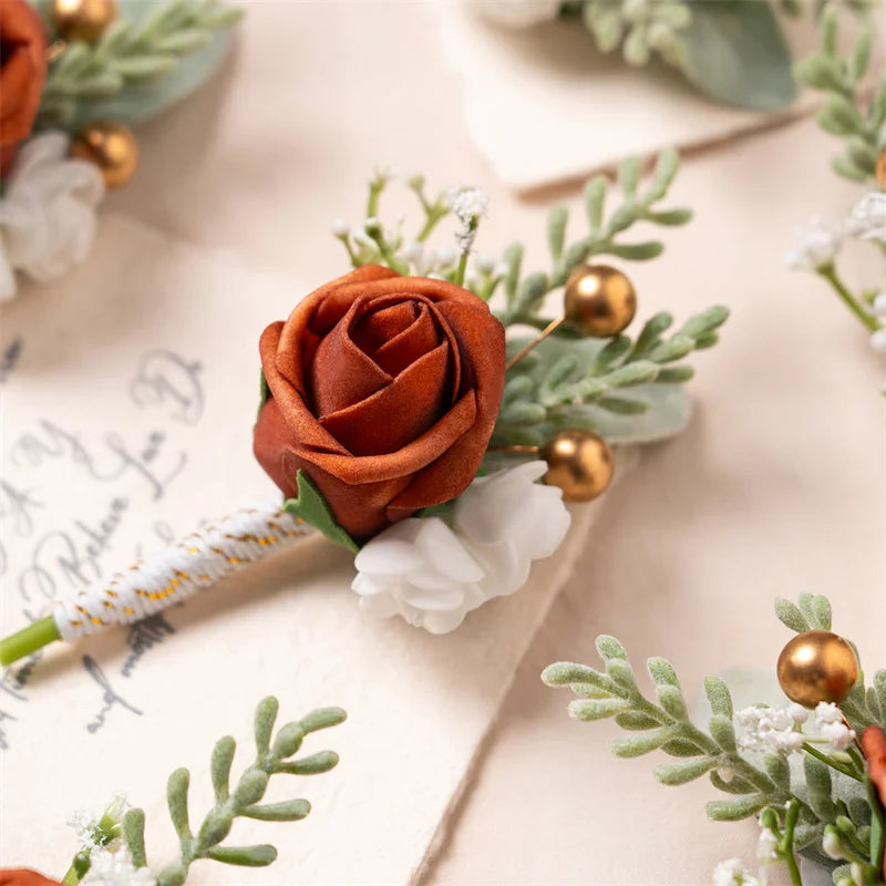 Boutonnière en soie orange vintage avec des fleurs blanches et du feuillage vert sur fond clair.