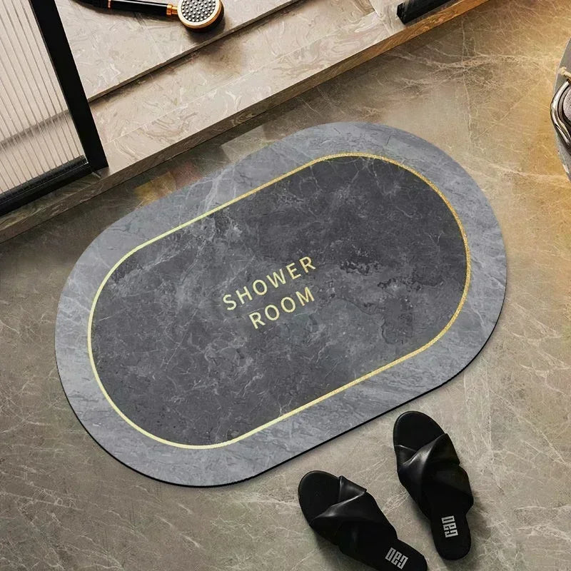 A round, dark gray bath mat with a gold rim is placed on a stone surface next to a pair of black flip-flops.