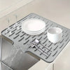 A silicone dish drying mat with raised drainage ridges holds a stack of white plates and a bowl.