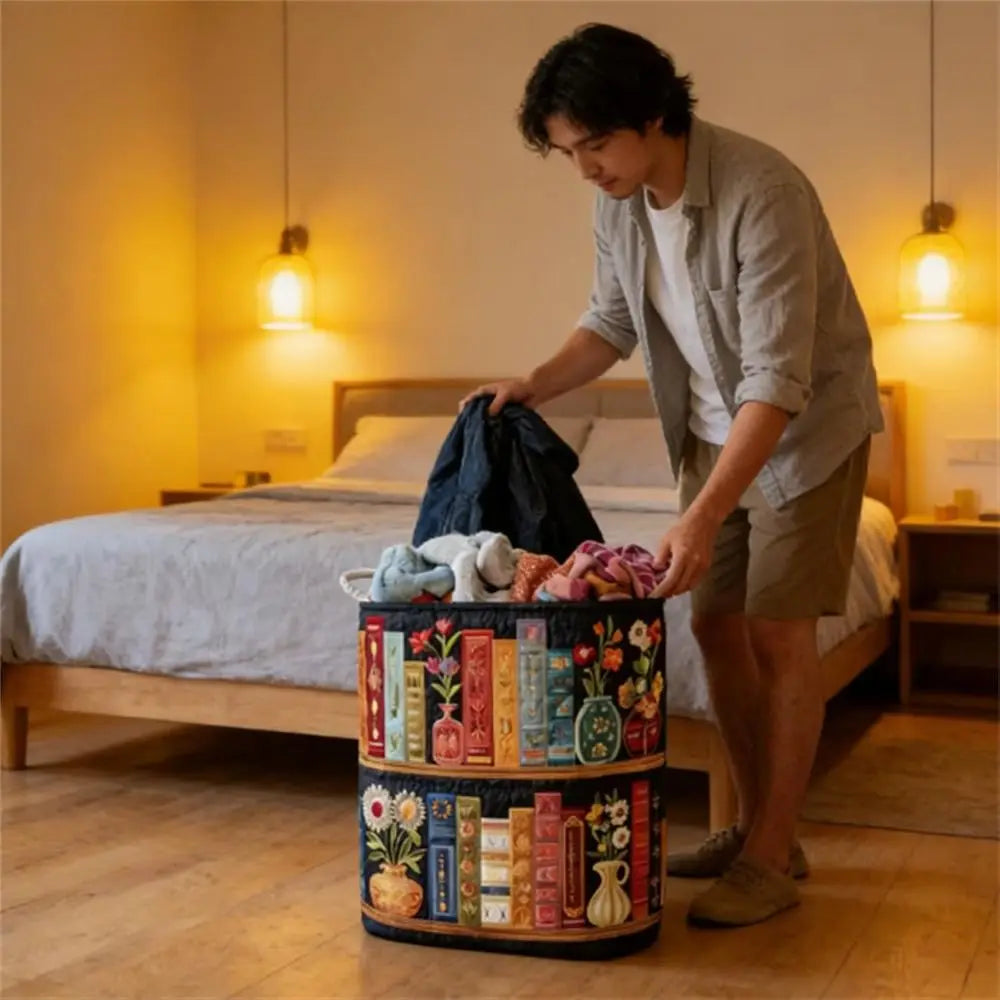 A person is holding a stack of folded laundry in a tiered floral storage basket next to a bed.