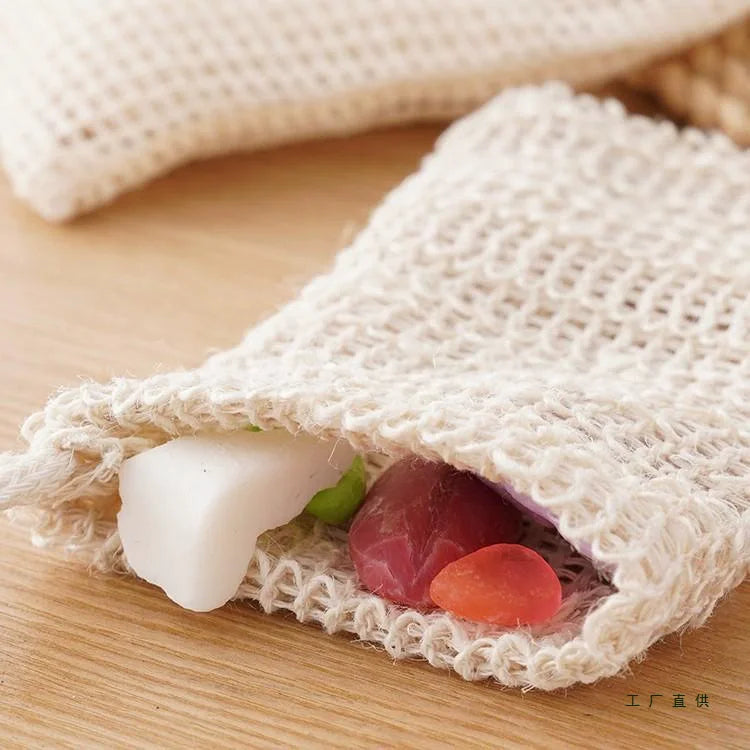 Handgemachte Sisal-Seife-Säckchen mit Naturseifen und grünen Blättern auf Holz