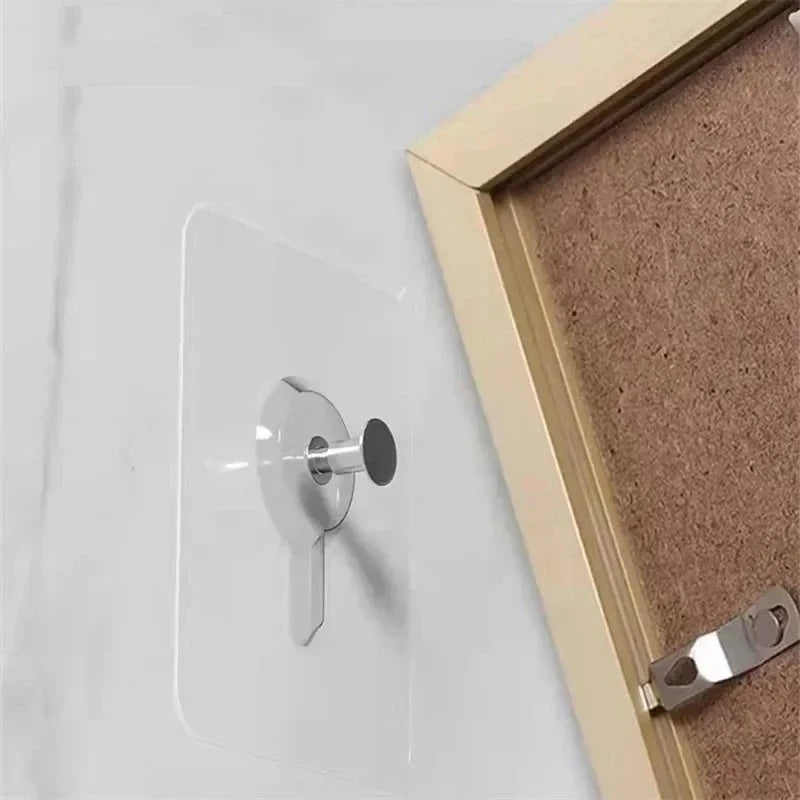 A transparent self-adhesive wall hook is installed on a white wall next to a wooden picture frame.