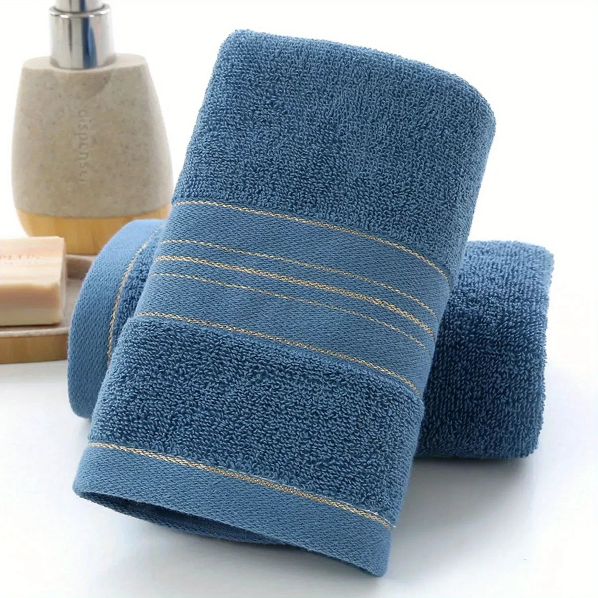 A dark blue bath towel with gold trim is shown next to a wooden soap dispenser.