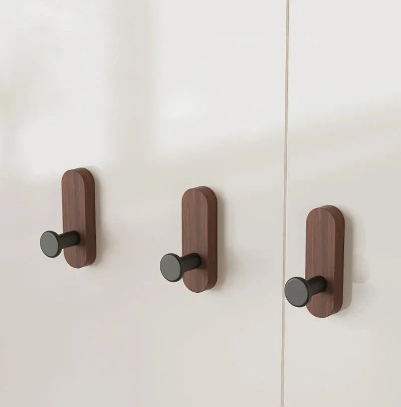 Three walnut wood wall hooks with black mounting plates are shown against a light wall.